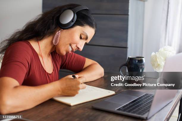 lächelnde frau, die musik hört, während sie von zu hause aus arbeitet - how we listen to music stock-fotos und bilder