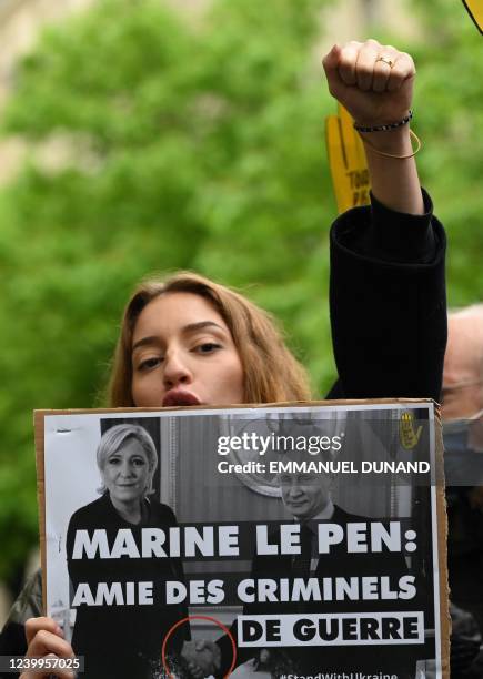 Protester holds a photo of French far-right Rassemblement National party Member of Parliament and presidential candidate Marine Le Pen shaking hands...