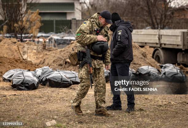 Graphic content / A member of the Ukrainian army and a policeman stand near body bags exhumed from a mass grave where civilians where buried in...