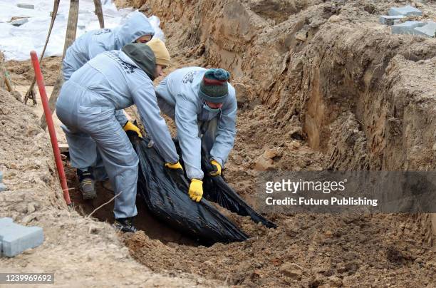 Experts in protective suits pull a human remains pouch out of another mass grave where civilians killed by Russian invaders are buried during...