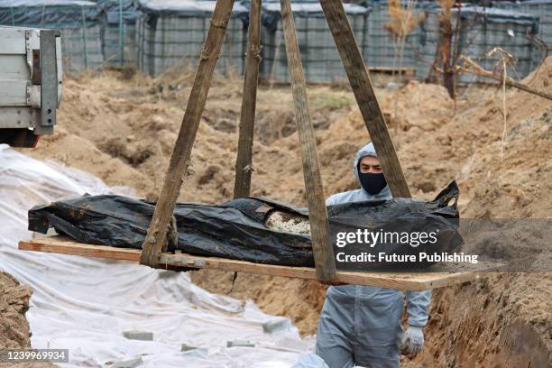 An expert in a protective suit watches a human remains pouch with a late person being lifted out of another mass grave where civilians killed by...