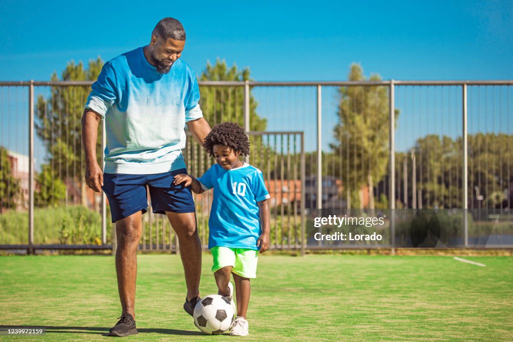 Pai negro e filho jovem treinando no campo de futebol