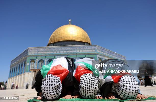 Palestinian girls, wearing national flags and checkered 'kafiyeh' headdresses kneel to pray in front of the Dome of Rock mosque at the al-Aqsa mosque...