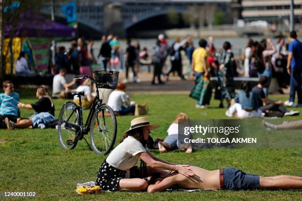 Woman applies some sunscreen to her partner as they sunbathe outside Tate Modern on the south bank of the River Thames in London on April 15 as the...