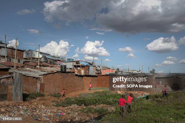 Kids play by the streets with a background view of housing structures in Kibera.