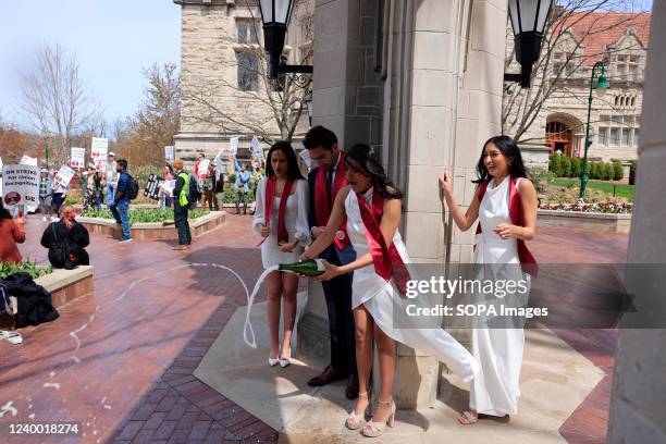 Group of graduating students opened a bottle of Champagne during a photo session at the Sample Gates as members of the Indiana Graduate Workers...