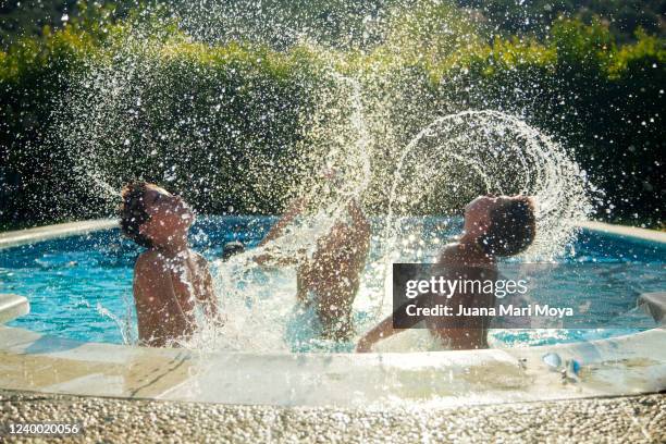 three children making crests with splashing water in a swimming pool - lido stock pictures, royalty-free photos & images