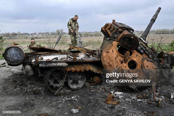 Ukrainian servicemen look at a destroyed Russian tank on a road in the village of Rusaniv, in the Kyiv region on April 16, 2022. - Many of the nearly...