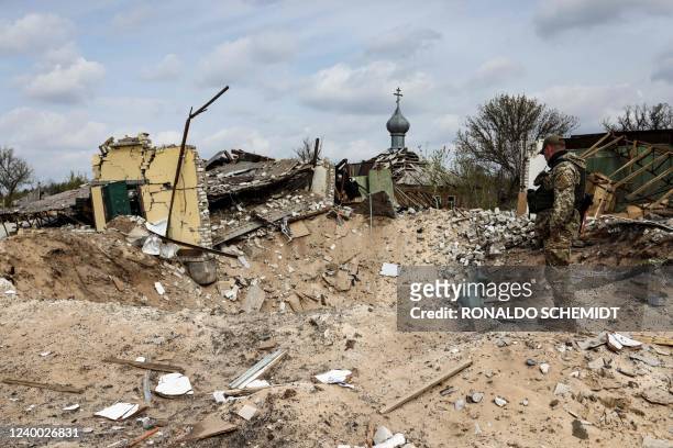 Ukranian serviceman looks into a crater and a destroyed home are pictured in the village of Yatskivka, eastern Ukraine on April 16, 2022. - Russia's...