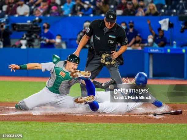 Raimel Tapia of the Toronto Blue Jays is safe at a play at home against Sean Murphy of the Oakland Athletics in the first inning during their MLB...