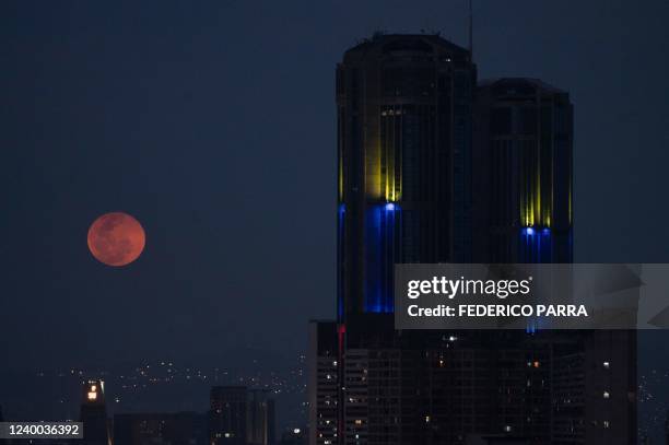 The full pink moon rises next to the Central Park tower in Caracas, on April 16, 2022.