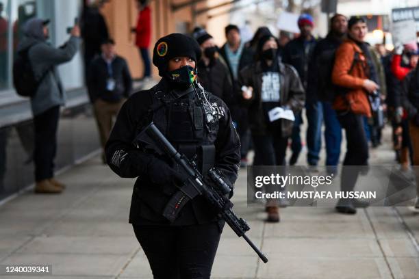 An armed woman providing protection for protesters, according to organizers, walks near protesters during a march for Patrick Lyoya, a Black man who...