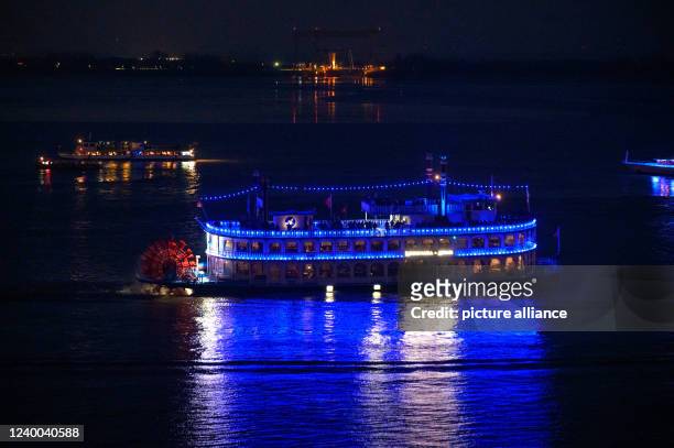 April 2022, Hamburg: The blue illuminated paddle steamer Louisiana Star sails along the Elbe in front of Blankenese at night. In many places, the...