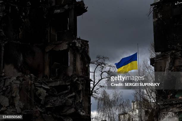 The Ukrainian flag flutters between buildings destroyed in bombardment, in the Ukrainian town of Borodianka, in the Kyiv region on April 17, 2022. -...