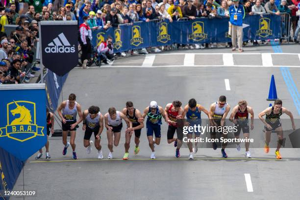 Runners in the men's professional race cross the starting line of the BAA Invitational Mile while a large crowd gathers to watch near the Boston...