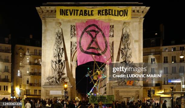 This photograph taken on April 17, 2022 shows Extinction Rebellion group's banners displayed on the Porte Saint Denis in central Paris. - Activists...