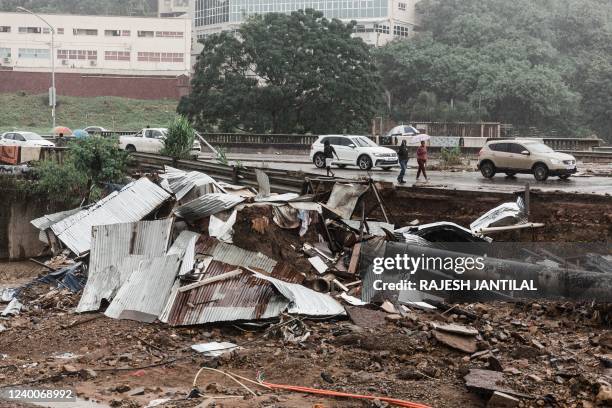 People walk pass the Quarry road informal settlement outside Durban on April 18, 2022 as rain begins to fall once again after winds, heavy rainfall...