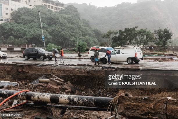 People walk pass the Quarry road informal settlement outside Durban on April 18, 2022 as rain begins to fall once again after winds, heavy rainfall...