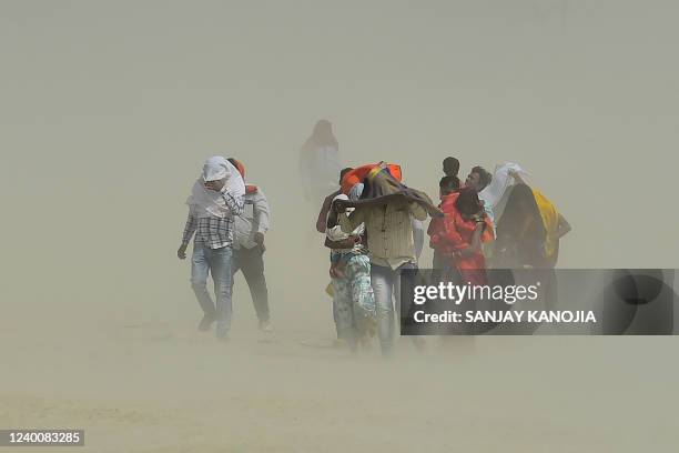 People walk through a sand storm at the Sangam, the confluence of the rivers Ganges, Yamuna and mythical Saraswati in Allahabad on April 19, 2022.