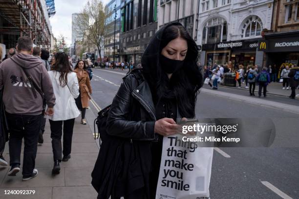 Shopper wearing a face mask carrying a bag which reads 'things that make you smile' out on Oxford Street on 13th April 2022 in London, United...