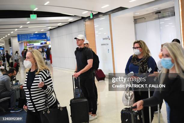 Airline passengers, some not wearing face masks following the end of Covid-19 public transportation masking rules, wait to board an American Airlines...