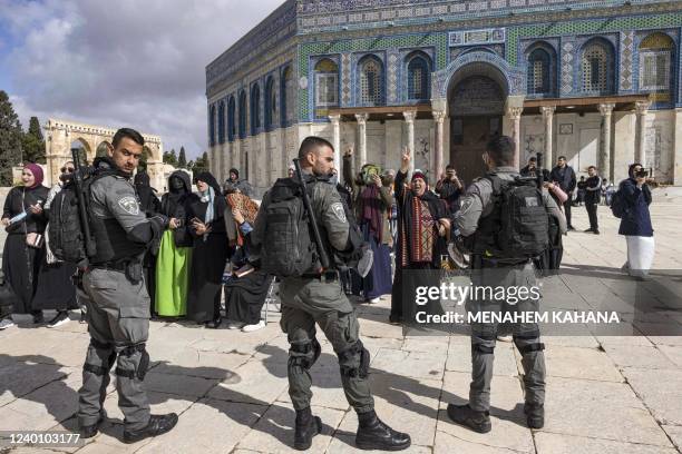 Israeli policemen stand guard in front of Muslim women praying in front of the Dome of the Rock mosque as a group of religious Jewish men and women...