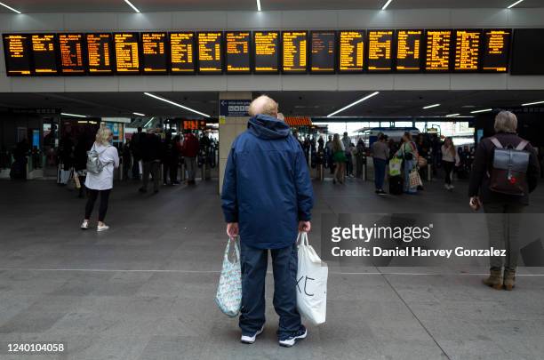 Members of the public, one a man carrying two carrier bags, checks train times on the digital timetable overhead as the government's Transport...