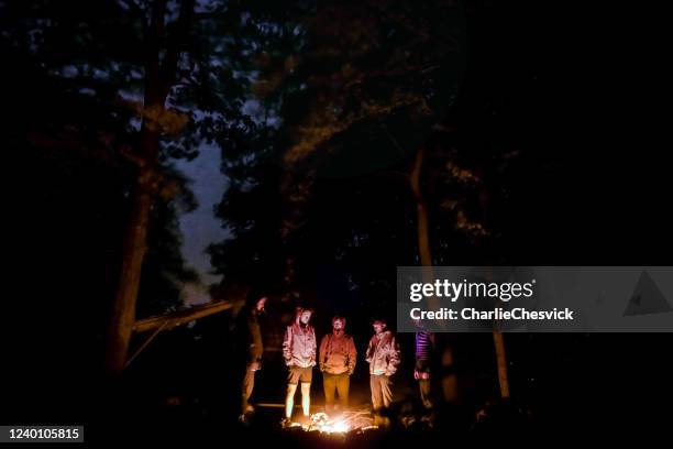 group of men, backpackers, tourist standing around campfire in forest under oak trees and sky is visible between trees white carpathians in czechia (carpathian mountain range) - camping campfire stock pictures, royalty-free photos & images