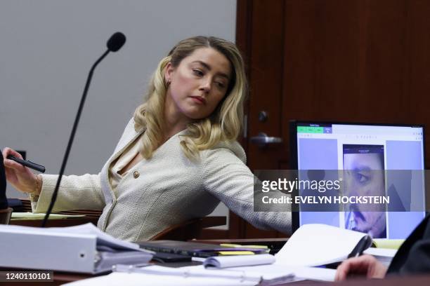 Actress Amber Heard listens to her ex-husband Johnny Depp, as a picture of an injury to his face is seen on a screen, during his defamation trial...