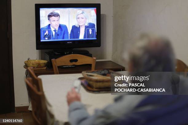 Man watches on TV a live televised debate between French President and La Republique en Marche party candidate for re-election Emmanuel Macron and...