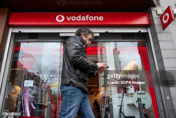 Pedestrian uses a smartphone as he walks past the British multinational telecommunications corporation and phone operator, Vodafone, store in Spain.