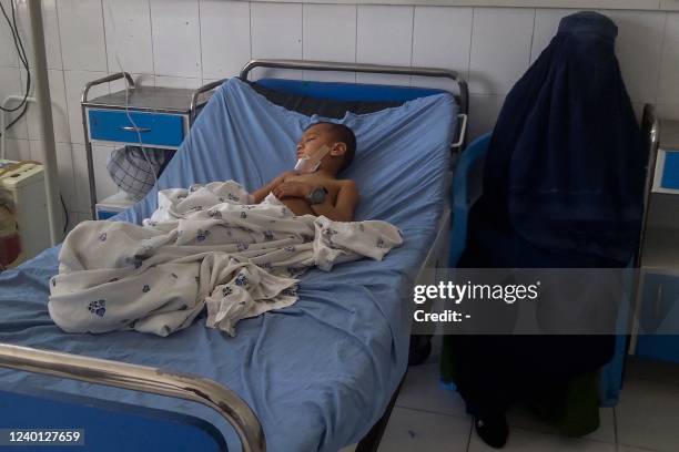 Burqa clad Afghan woman sits next to a child receiving treatment at a hospital after he got injured in a bomb blast in Kunduz on April 21, 2022.