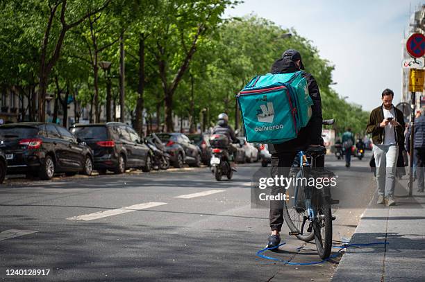 Cyclist with a 'Deliveroo' company bag pauses on a street in Paris on April 20, 2022. A Paris court on April 19, fined the British meal delivery...