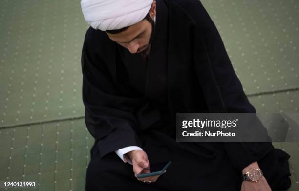 An Iranian cleric uses his smartphone as he sits at a prayer hall in the Imam Khomeini Grand mosque in downtown Tehran while waiting for the...