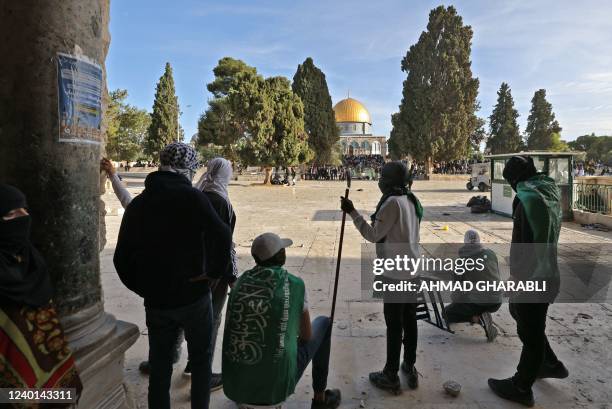 Palestinian youths, wrapped with the flag of the Islamic Hamas movement, take position in the courtyard of Jerusalem's Al-Aqsa mosques compound, with...