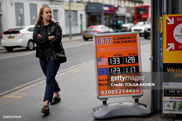 Pedestrina walks past a board indicating exchange currencies between the Sterling and the US Dollar and Euros, in Central London on April 22, 2022....