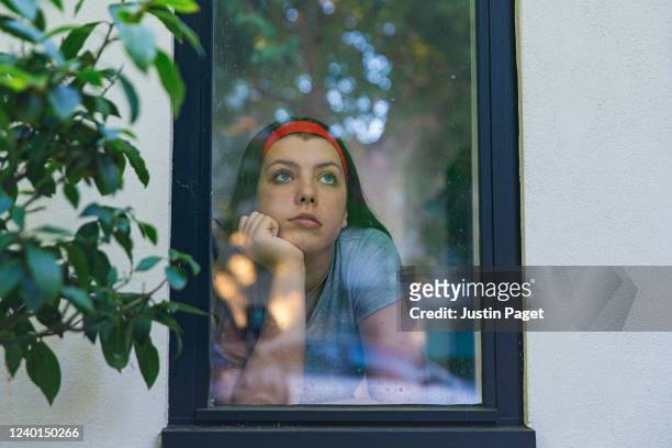 teenage girl looking through window - quarantäne stock-fotos und bilder