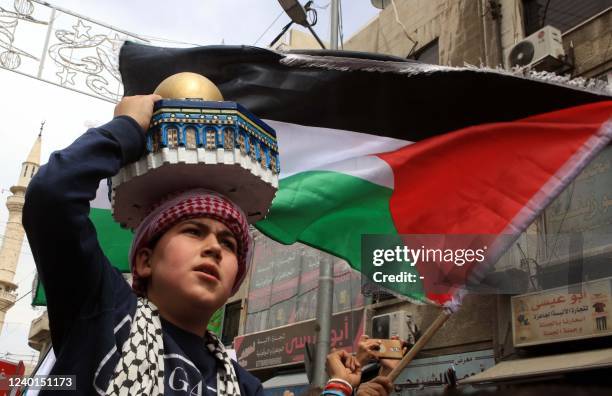 Young boy carries a replica of the Dome of the Rock mosque and waves a Palestinian flag as demonstrators march in the streets of the Jordanian...