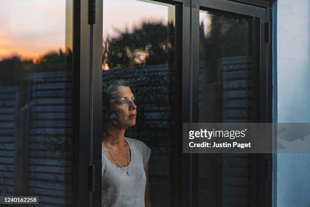 woman looking through window at dusk - isolamento foto e immagini stock