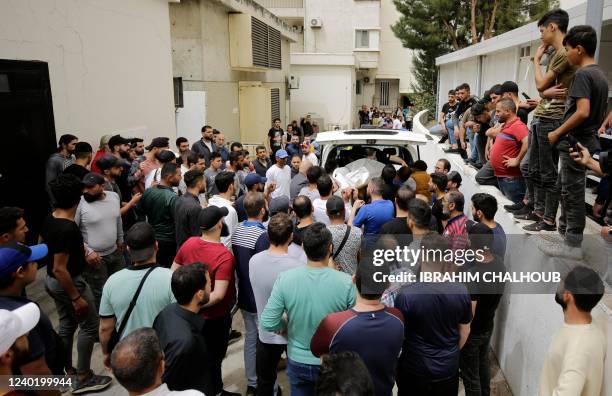People gather at the entrance of the morgue of a hospital in Tripoli, as others carry the body of one of the people who died when their boat capsized...