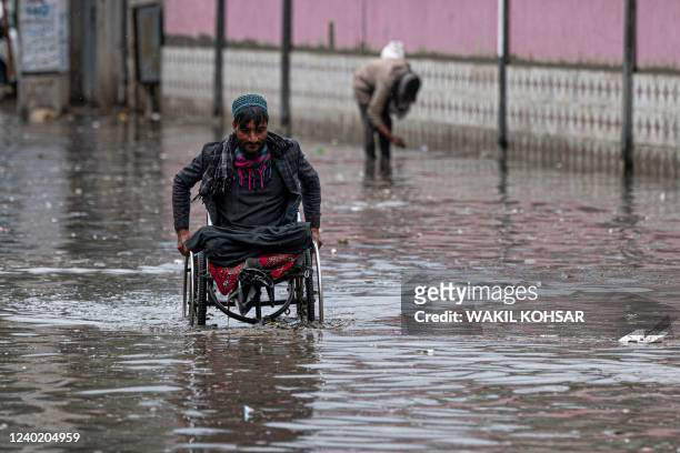 Man on a wheelchair makes his way through flood waters after heavy rains at the old section of Kabul on April 24, 2022.