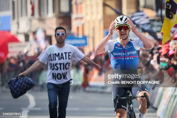 Protester wearing a tshirt follows Belgian Remco Evenepoel of Quick-Step Alpha Vinyl, who celebrates as he crosses the finish line to win the...