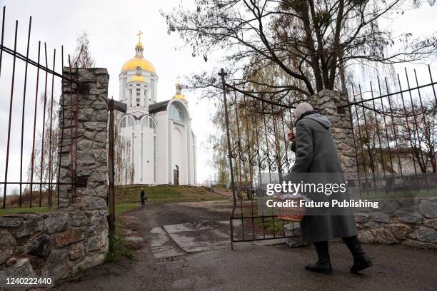 Woman carrying an Easter basket crosses herself before entering the premises of the Church of Saint Andrew the First-Called Apostle in Bucha that is...