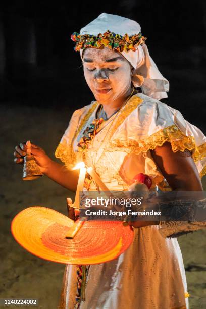 Bwiti cult follower with candles and ritual instruments during an initiation ceremony. In Bwiti ceremonies, participants cover their faces with a...