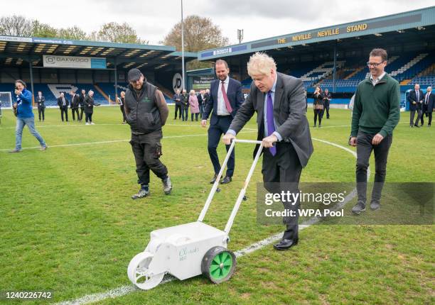 Prime Minister Boris Johnson paints over the white line of the centre circle during a visit to Bury FC at their Gigg Lane ground, on April 25, 2002...