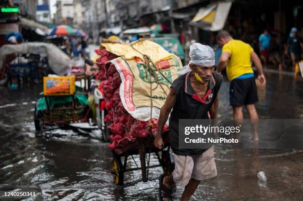 Worker carrying sacks of onions wades through a flooded street at a market in Manila, Philippines, on April 26, 2022.