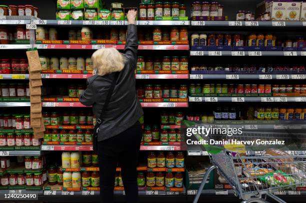 An older woman in an Asda superstore reaches past shelves of various pasta sauces, a common household staple, for the Dolmio brand sauce, as...