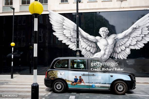 Black cab carrying advertising showing two young men enjoying a poolside holiday and the image of a mythical male hero, believed to be Icarus, on the...