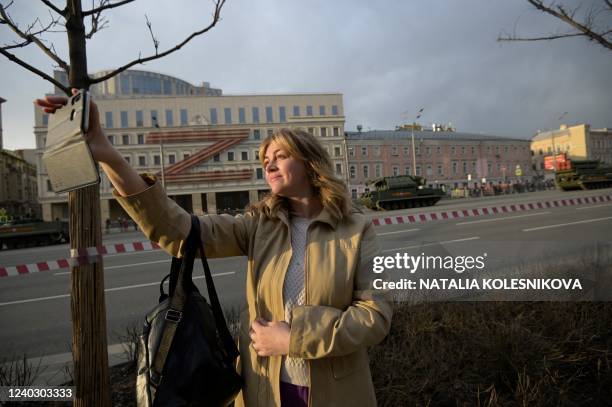 Woman uses her smartphone as she watches military vehicles driving along the Garden Ring road and heading to Red Square for a rehearsal of the...