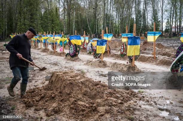 Man seen digging a grave with Ukrainian flags posted on graves in the background. Mass graves for bodies of people killed during the Russian...
